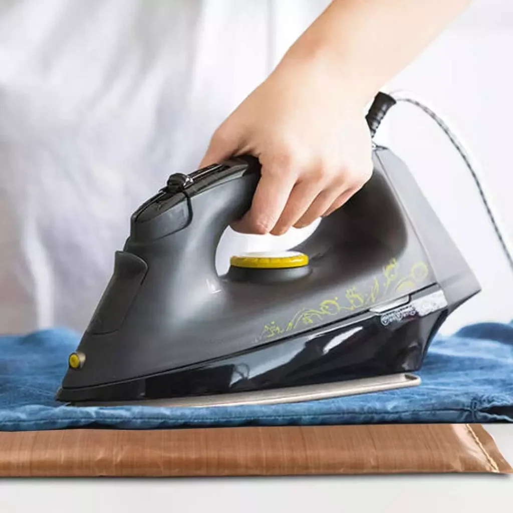 Wholesale heat press pillow mat kits being used with a handheld iron on denim fabric for precise vinyl transfer and garment crafting