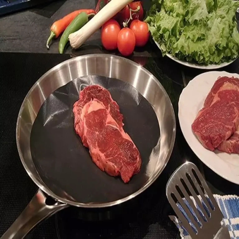 A premium black circular PTFE fryer pan liner placed flat inside a stainless steel skillet, seared with a beef steak for bulk wholesale.