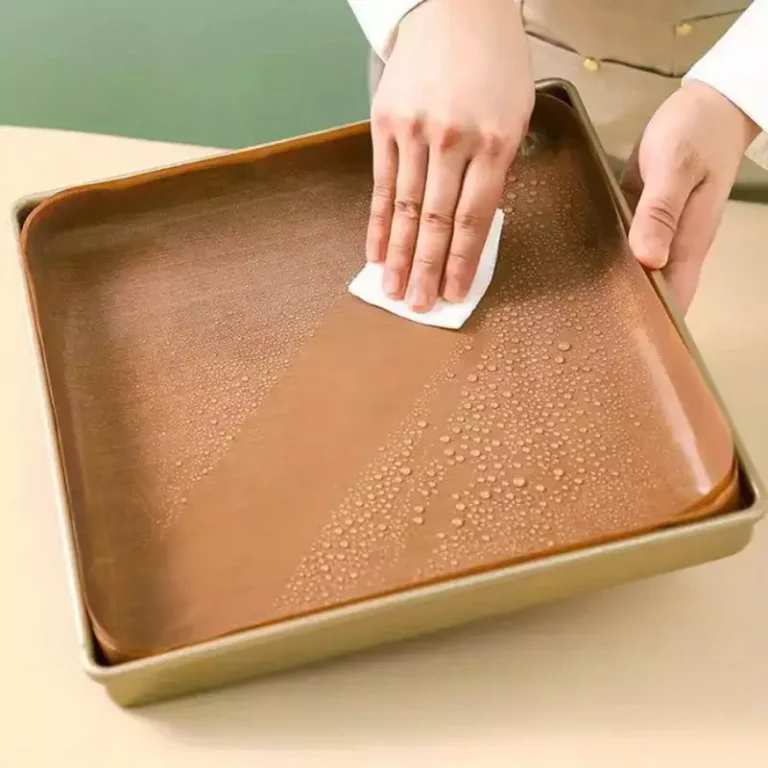 A premium brown PTFE square cake pan liner inside a metal baking tin being wiped clean by hands, demonstrating non-stick food grade finish.